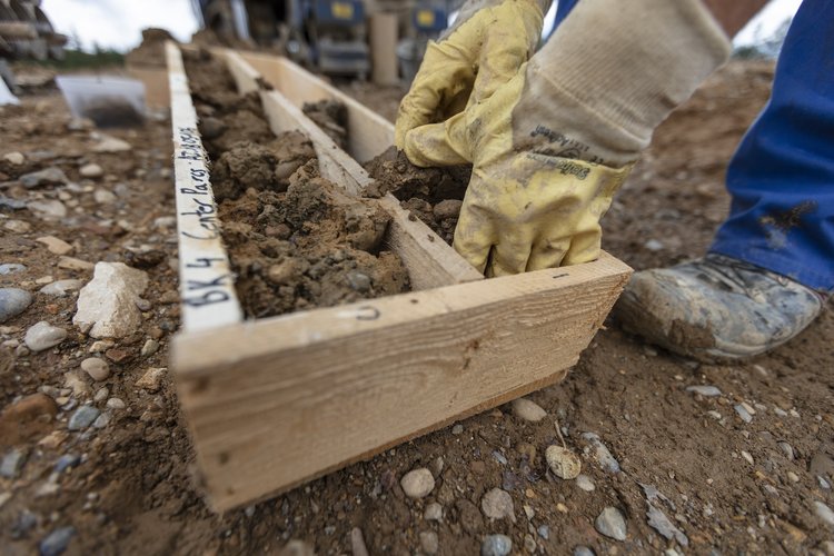 Eine Mitarbeiter von GHB Consult füllt Erdproben in einen langen, rechteckigen Holzrahmen für Baugrunduntersuchungen.