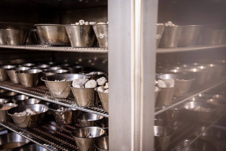 Mehrere Regalböden mit metallischen Schüsseln, Bodenmeschanisches Labor von GHB Consult , die mit kleinen weißen Steinen oder Erzeugnissen gefüllt sind, in einem Schrank oder Lagerregal.