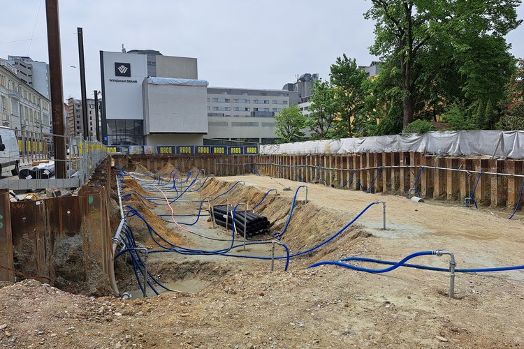 Baugrube auf einer Baustelle von GHB Consult, umgeben von Metallwänden und mit mehreren blauen Rohren, die im Boden verlaufen.
