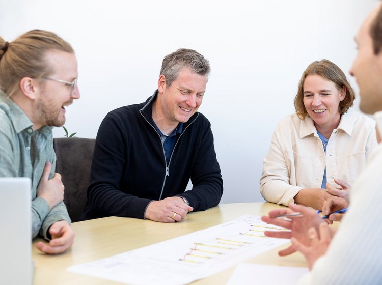 Vier Personen sitzen an einem Tisch und besprechen gemeinsam Pläne oder Dokumente. Alle wirken konzentriert und freundlich.
