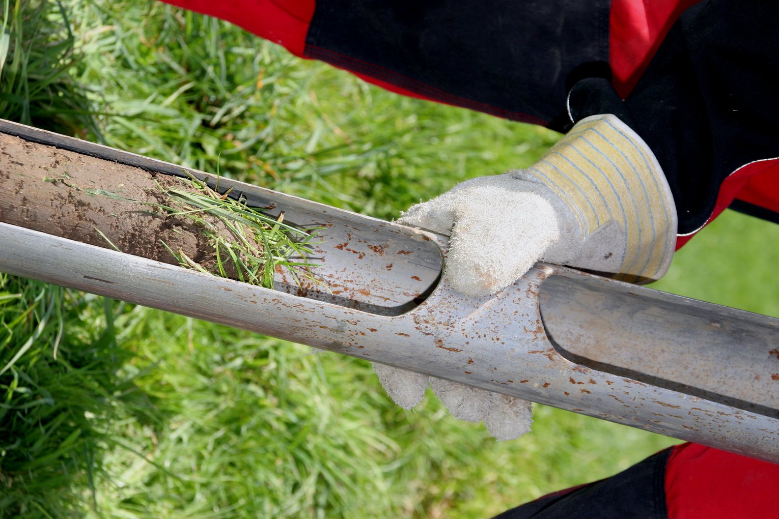Eine Mitarbeiter von GHB Consult mit Handschuhen hält eine Kehrbohrung auf einer Wiese in den Händen.