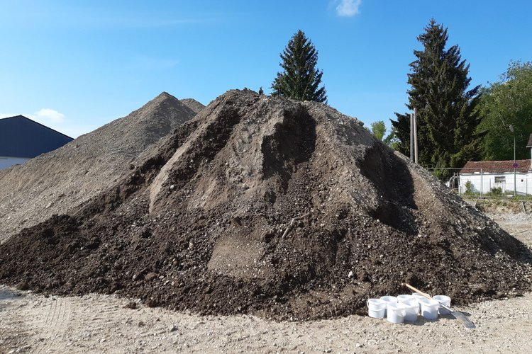 Großer Erdhaufen auf einer Baustelle, daneben mehrere weiße Plastikeimer. 