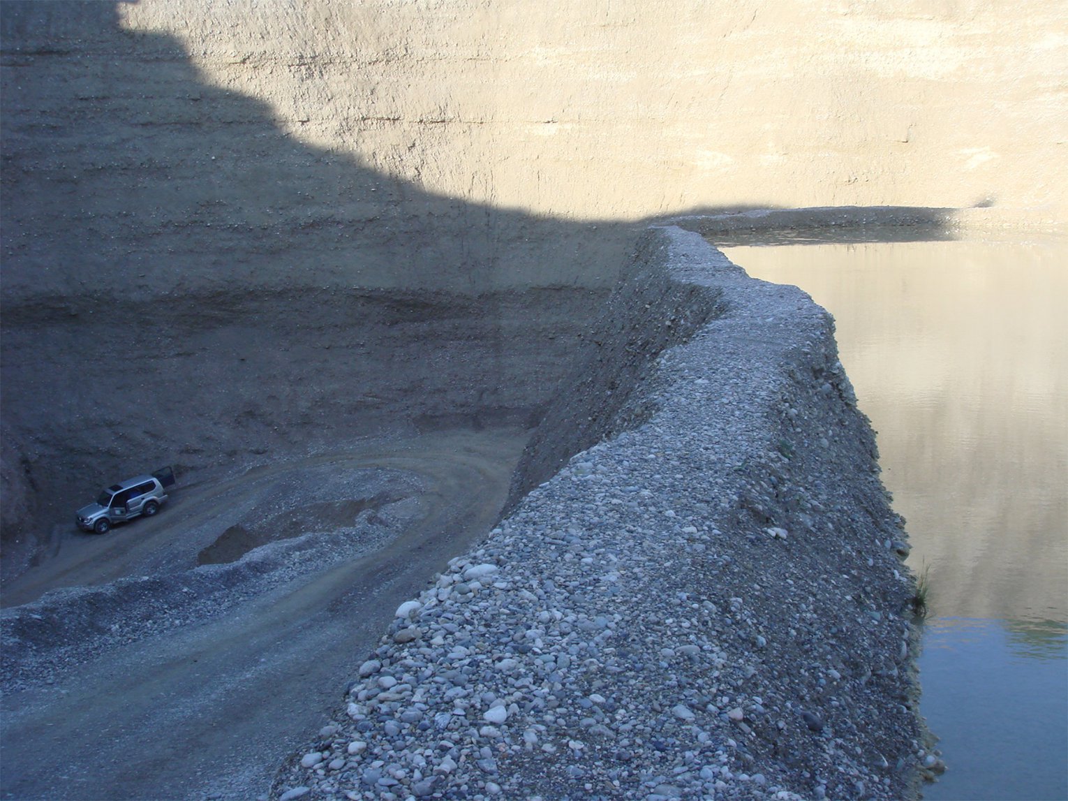 Ein Geländewagen fährt auf einer Schotterstraße in einem Steinbruch, rechts ist ein großes, mit Wasser gefülltes Becken.